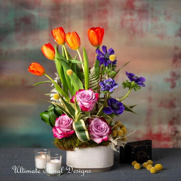 Arrangement of orange tulips, purple flowers, and pink roses in a white pot