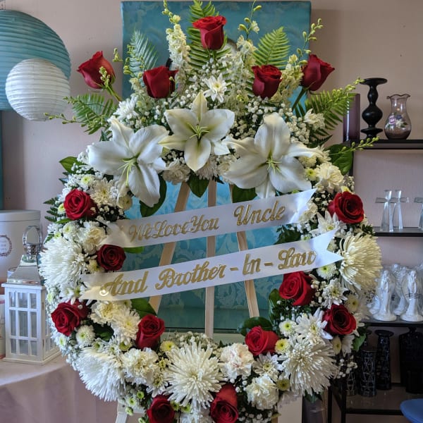 Large funeral wreath with red roses, white lilies, and white mums on an easel