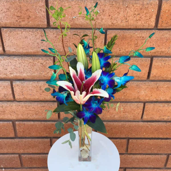 Pink and white lilies in a clear glass vase with blue flowers