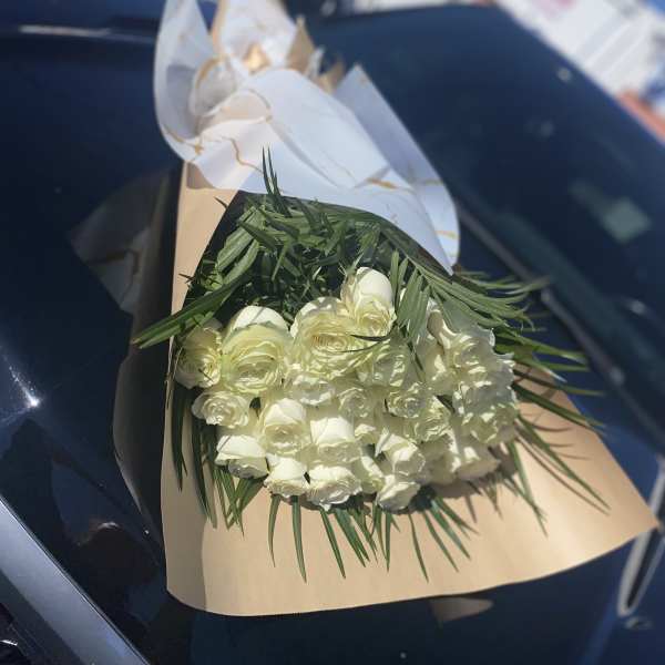Bouquet of white roses wrapped in tan paper with white ribbon