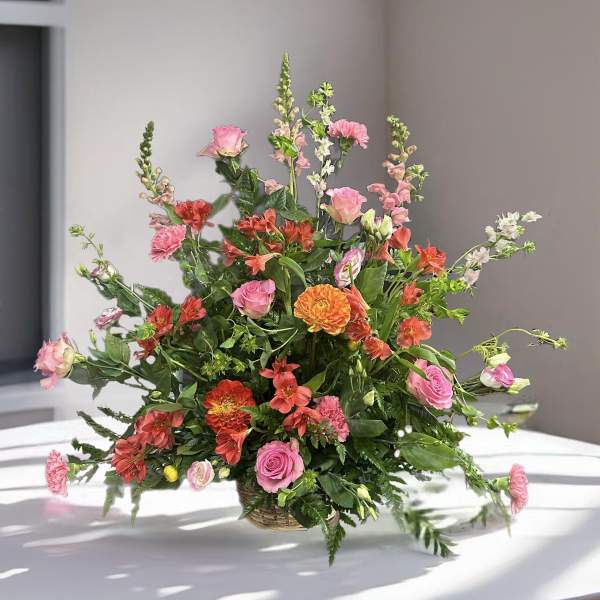 Mixed pink and orange flowers in a low basket arrangement