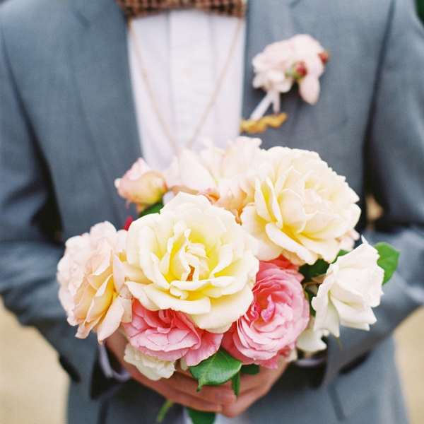 Man holding a bouquet of pale pink and cream roses with a boutonniere on his jacket