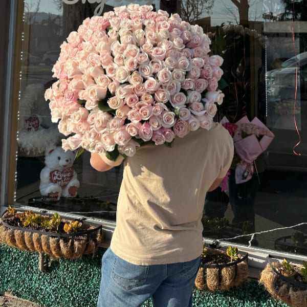 Large bouquet of pale pink roses held in front of a shop window