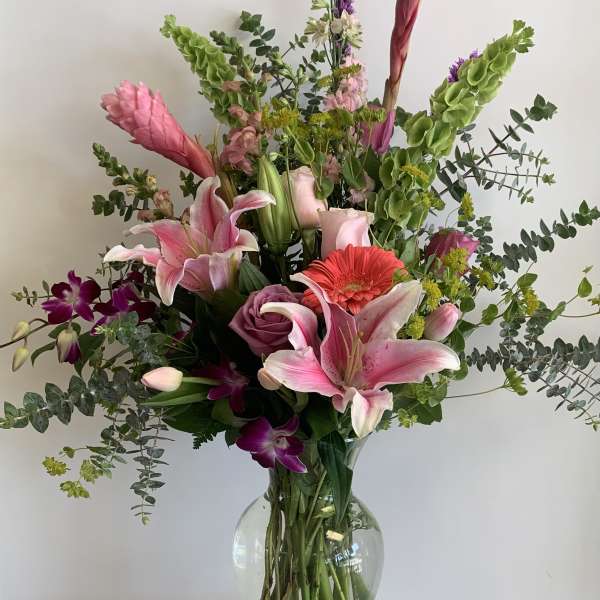 Mixed bouquet of pink lilies, roses, and orchids in a glass vase