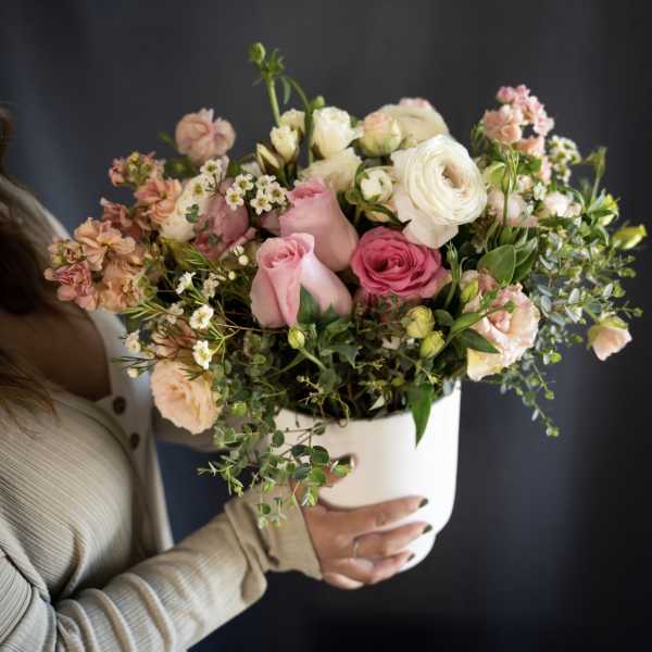 Handheld bouquet of pink and white roses in a white container