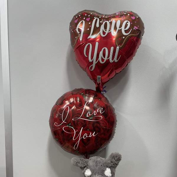 Two heart-shaped love balloons with a plush dog and chocolate candy bag