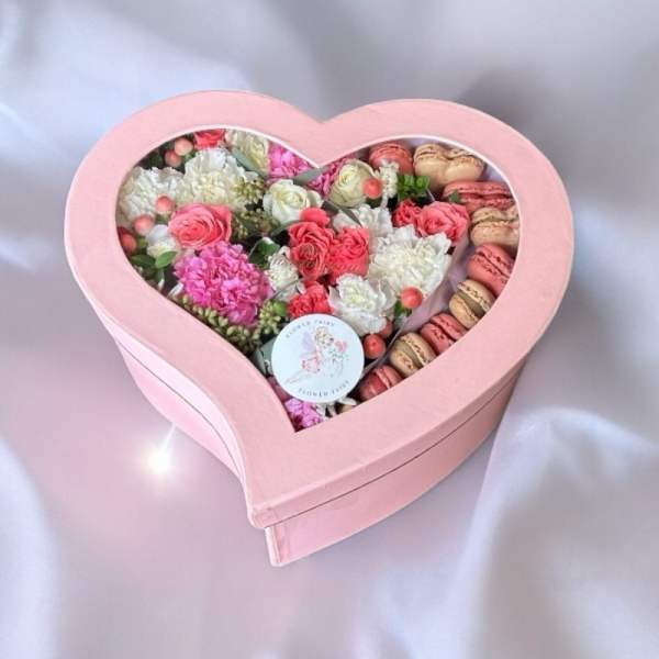 Heart-shaped pink box filled with pink and white flowers and macarons