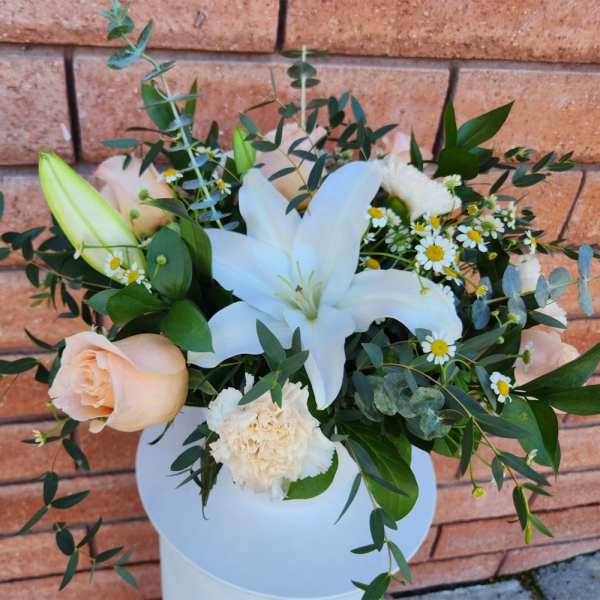 Arrangement of white lilies, peach roses, and small daisies in a white vase