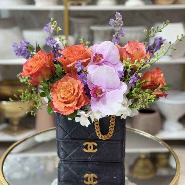Orange roses and pink orchids arranged in a black handbag-shaped box