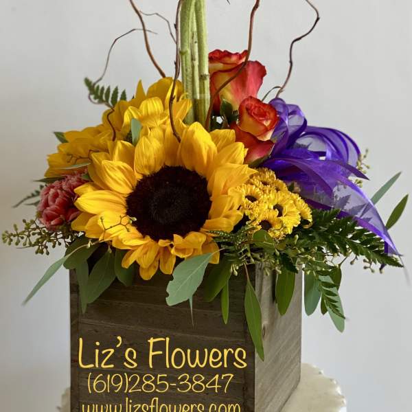 Sunflower arrangement in a wooden box with purple ribbon and roses