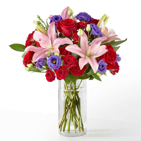 Bouquet of red roses, pink lilies, and purple blooms in a clear glass vase