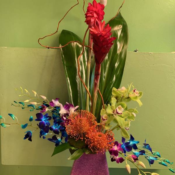 Tall tropical flower arrangement in a pink vase with red and blue orchids