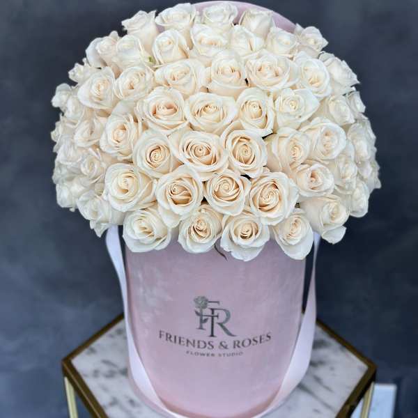 Cream roses arranged in a pink hat box with ribbon handles