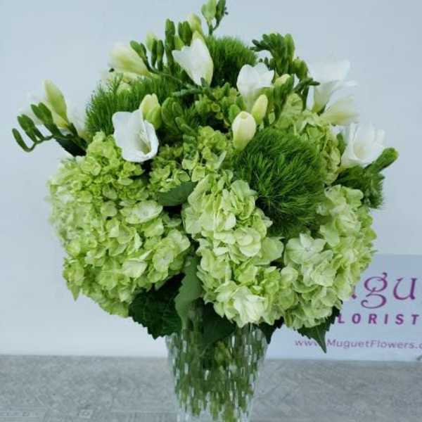 Green and white floral arrangement in a clear glass vase