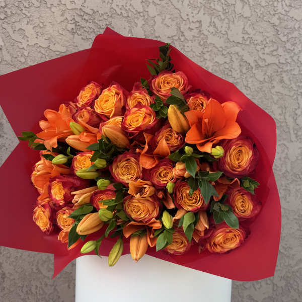 Bouquet of orange roses and lilies wrapped in bright pink paper