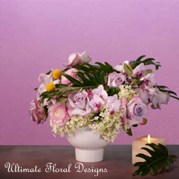 Lavender and pink floral arrangement in a white vase with a lit candle