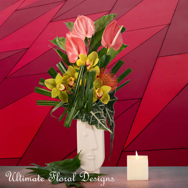 Tropical flower arrangement in a white face vase beside a candle