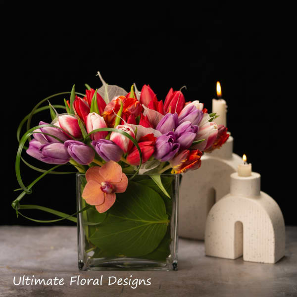 Colorful tulip arrangement in a square glass vase with candles nearby