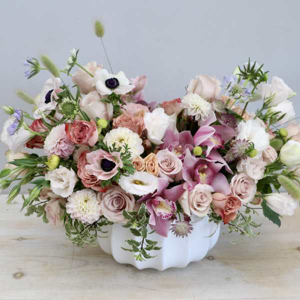 Low white bowl filled with pastel pink, peach, and white flowers including roses, orchids, and anemones.