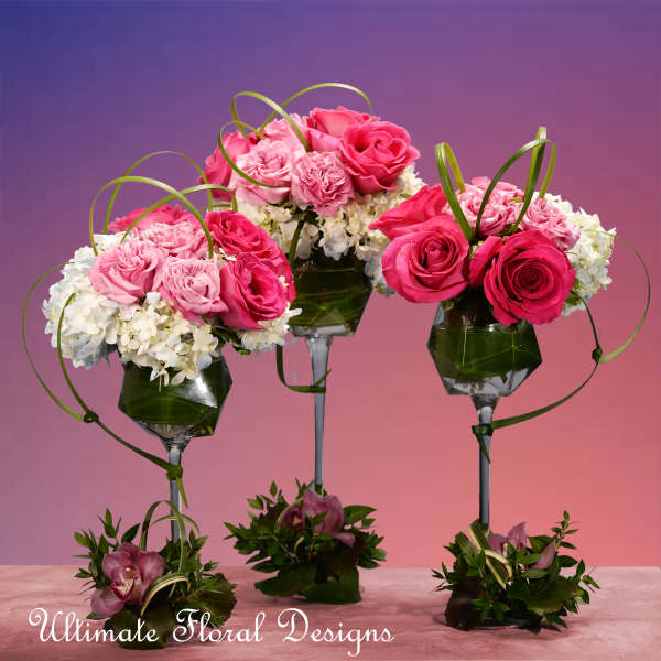 Three pink rose arrangements in tall glass holders with ribbon loops.