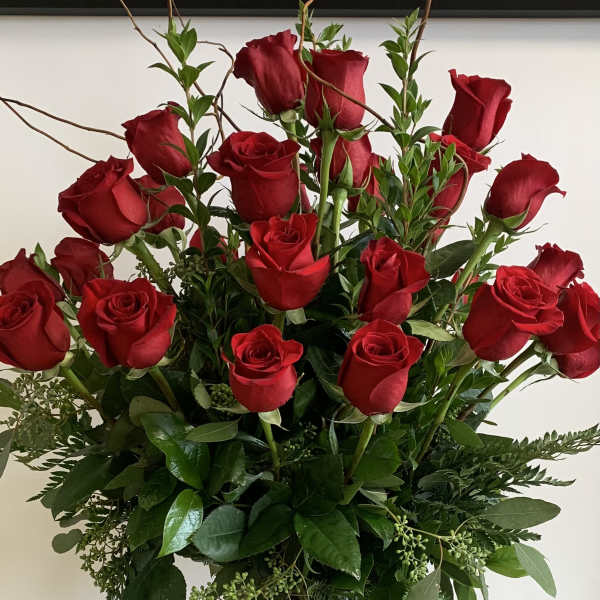 Tall vase arrangement of red roses with mixed greenery