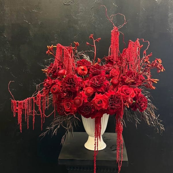 Red floral arrangement in a white pedestal vase