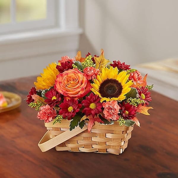 Basket of mixed flowers with a sunflower and rose on a table