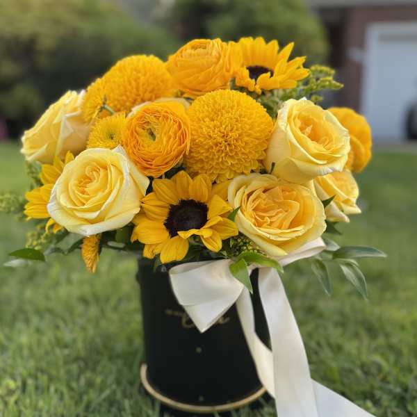 Yellow bouquet of roses and sunflowers in a black hatbox with a white ribbon