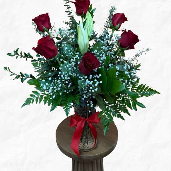 Red roses and a white lily in a glass vase with a red ribbon