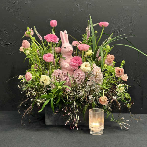 Pink floral arrangement with a rabbit figurine and a glass candle holder