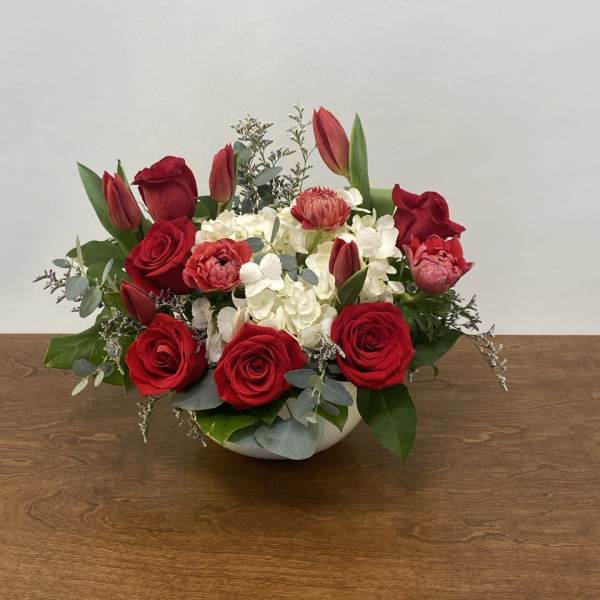 Red roses and tulips arranged with white hydrangeas in a low white bowl