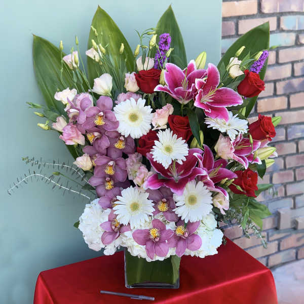 Mixed bouquet in a glass vase with pink lilies, red roses, orchids, and white daisies