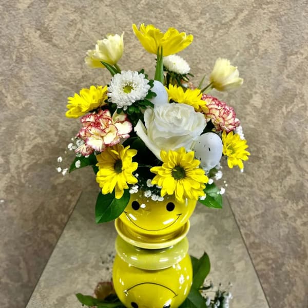 Yellow and white flower arrangement in a smiley-face vase