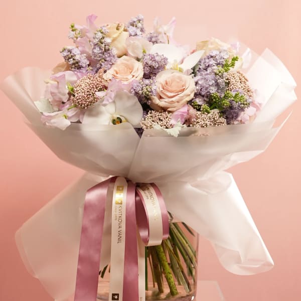 Pastel bouquet of roses, orchids, and lilac wrapped in white paper