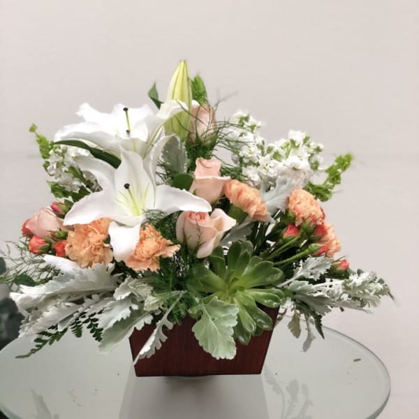 Arrangement of white lilies, peach roses, and carnations in a wooden container