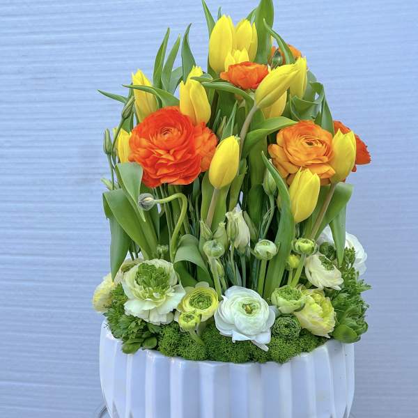 Yellow tulips and orange ranunculus in a white vase