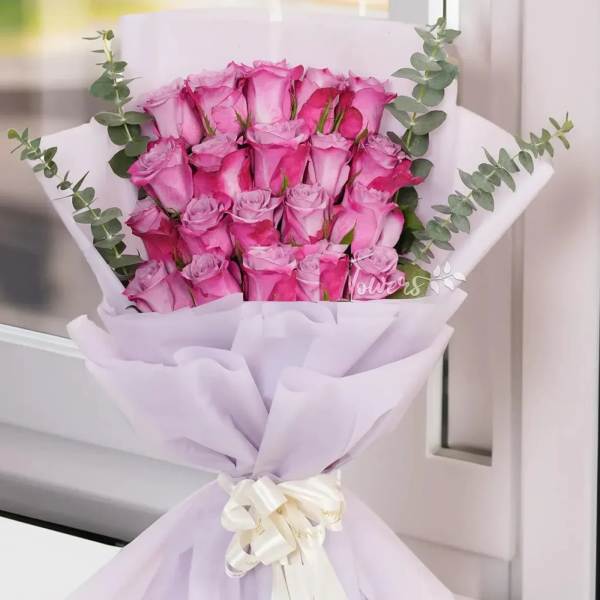 Bouquet of pink roses wrapped in pale lavender paper with a white ribbon
