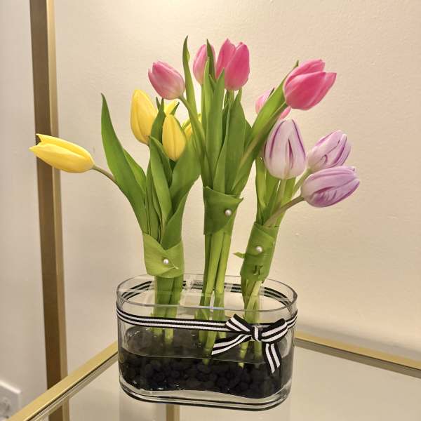 Three small tulip bundles in a clear glass vase with black stones