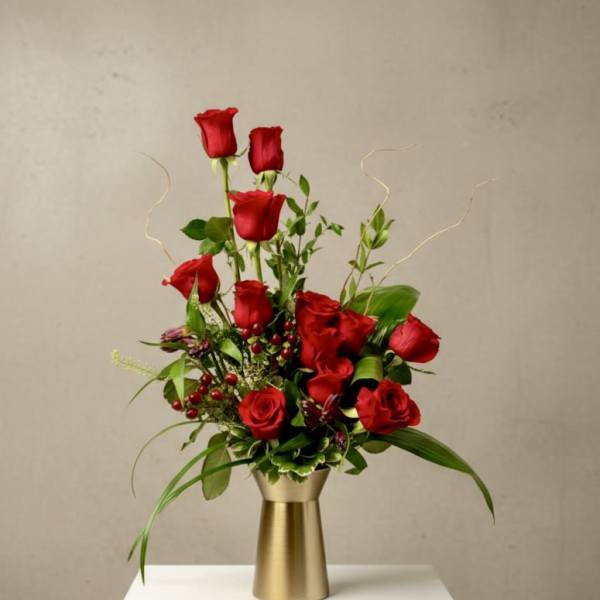 Red roses arranged in a gold vase with greenery