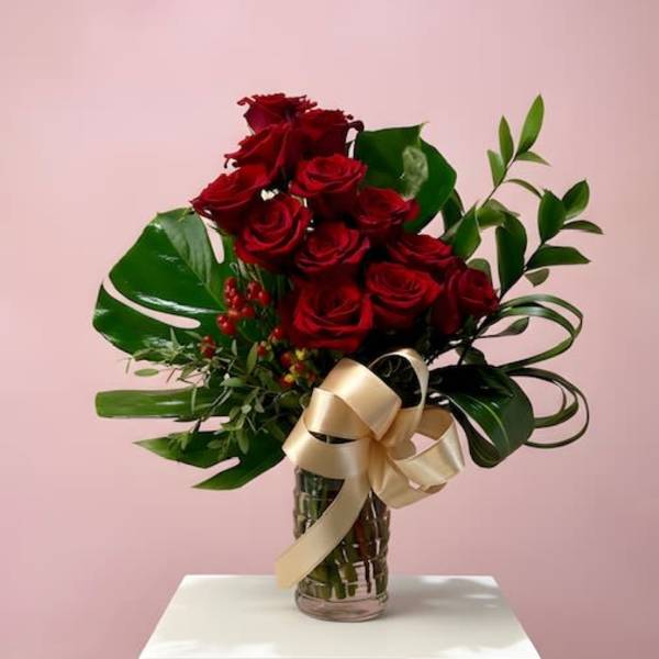Tall arrangement of red roses with tropical green leaves in a clear vase with a gold bow.