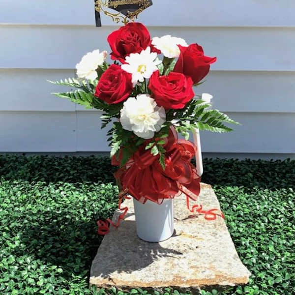 Red and white rose bouquet in a white vase with a graduation cap topper