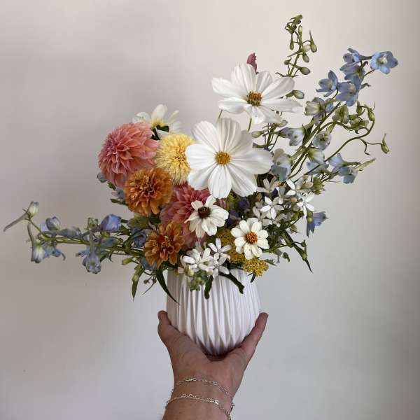 Mixed bouquet in a white ribbed vase with white, pink, orange, and blue flowers