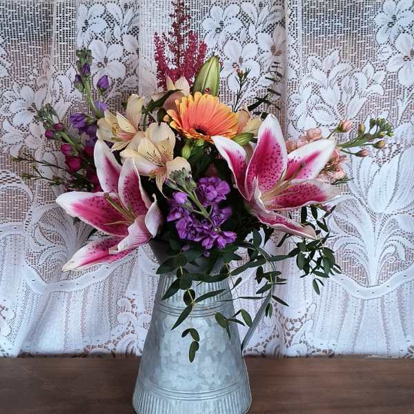 Pink lilies and mixed flowers arranged in a metal pitcher vase