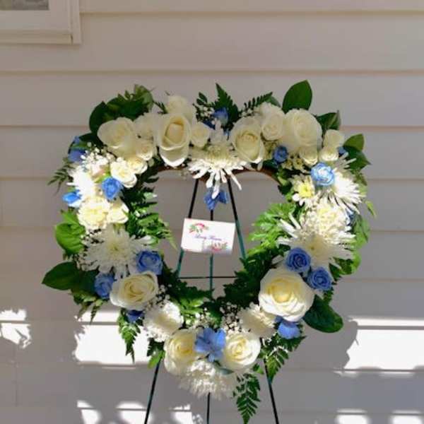 Heart-shaped floral wreath on a stand with white and blue flowers
