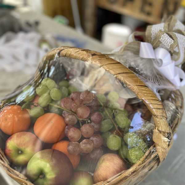 Gift basket of apples, oranges, and grapes wrapped in cellophane with a decorative bow