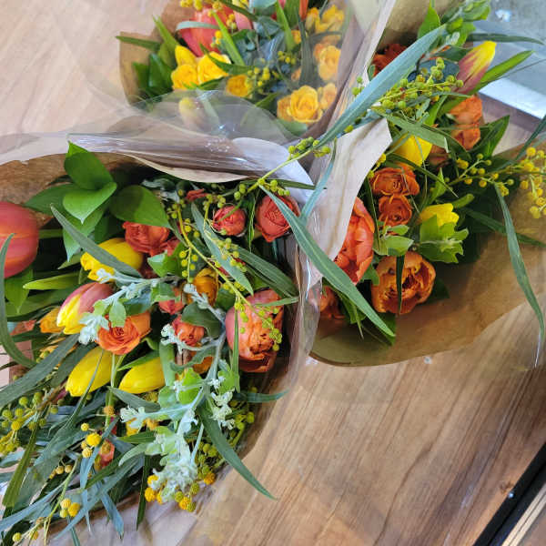 Three wrapped bouquets of orange and yellow tulips with greenery