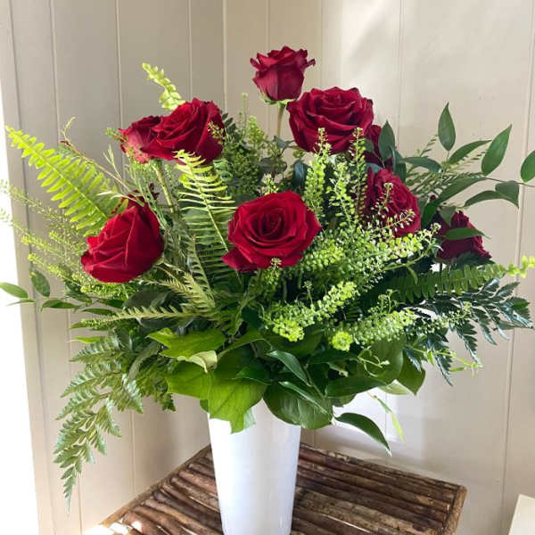 Red roses arranged in a white vase with mixed greenery