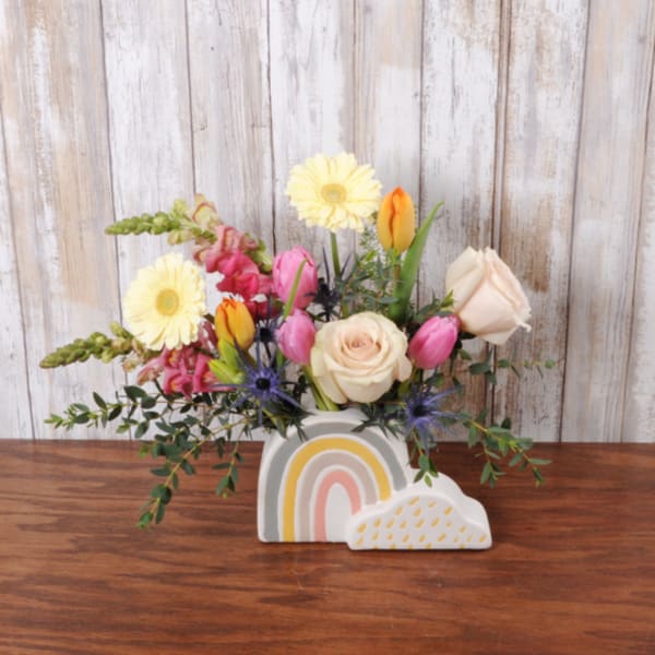 Short pastel flower arrangement in a rainbow-shaped ceramic container