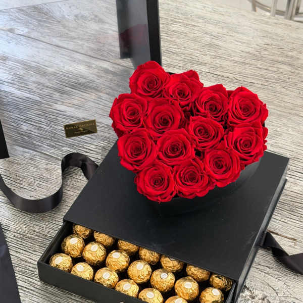 Heart-shaped red rose arrangement on a black gift box with gold chocolates