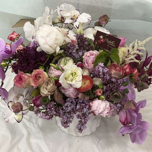 Mixed bouquet of purple, pink, and white flowers in a white container